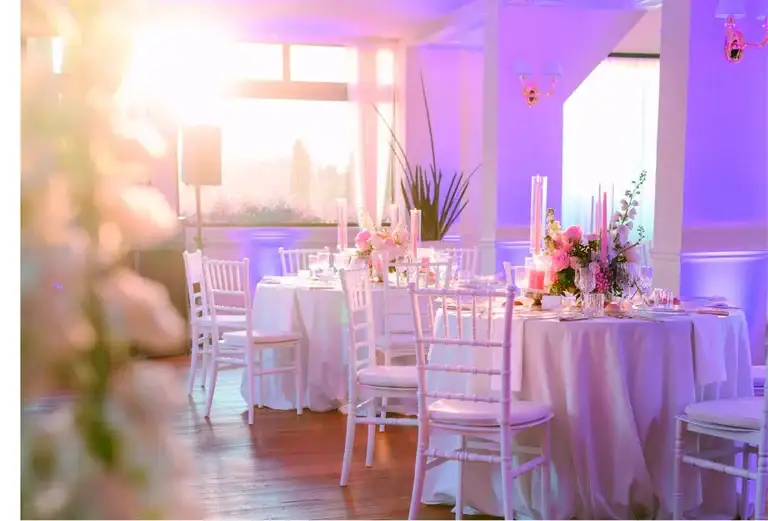 Indoor wedding reception with round tables, white Chiavari chairs and blush florals at sunset