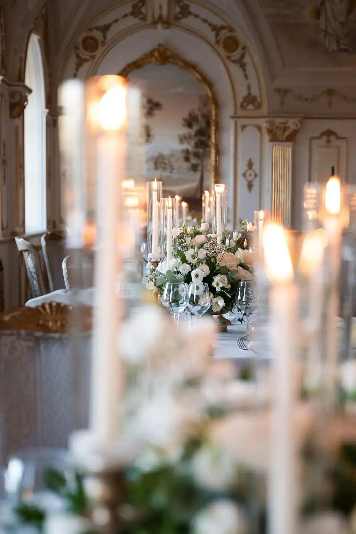 Banquet table in a frescoed villa hall with tall taper candles and white-rose centerpieces