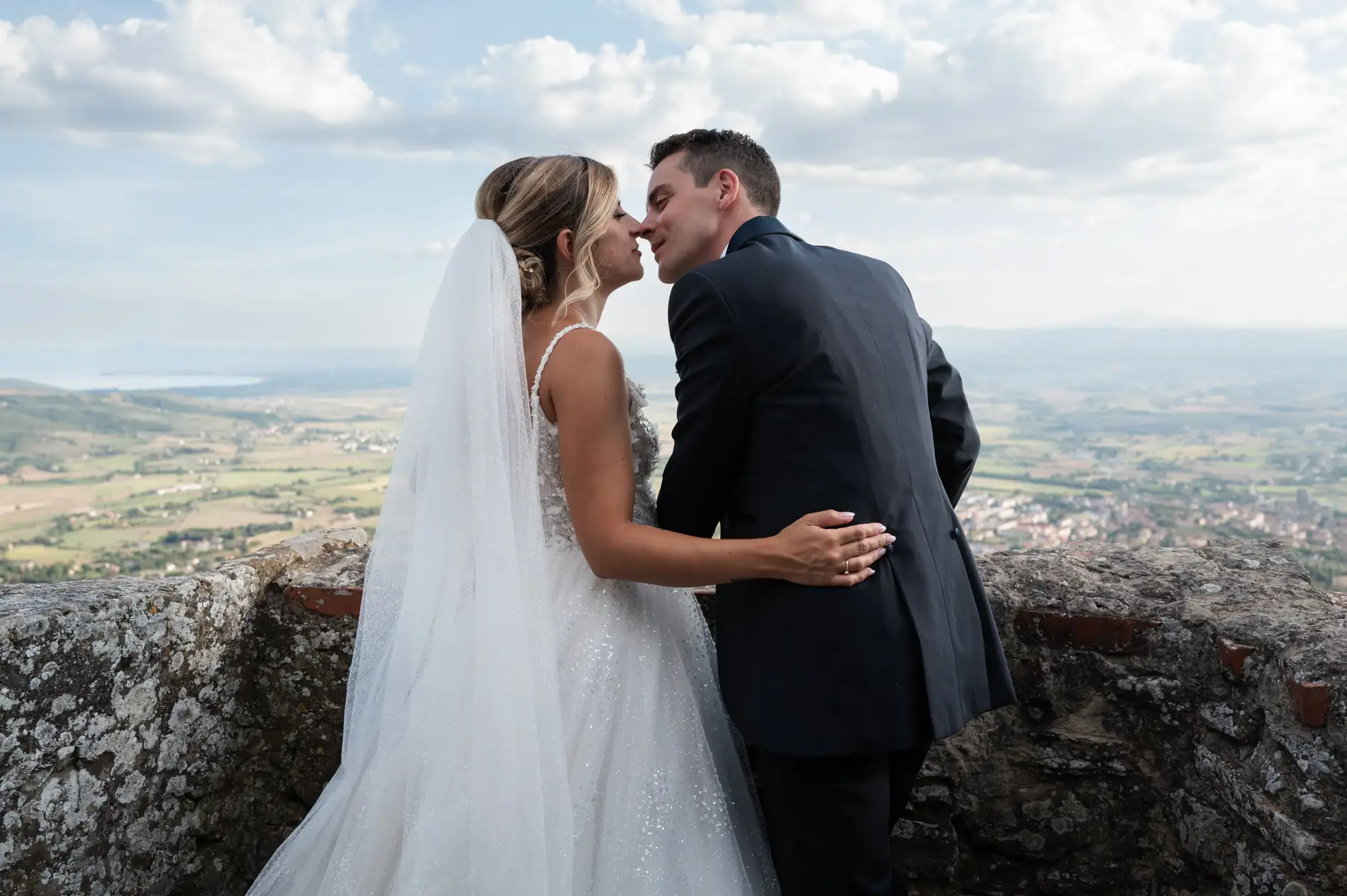 Bride and groom about to kiss on a stone terrace overlooking the Tuscan countryside and lake