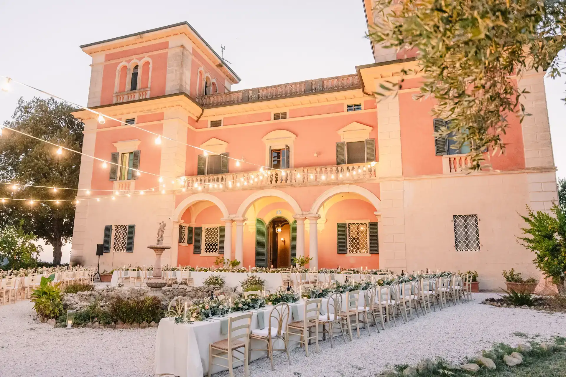 Historic terracotta Italian villa with an outdoor wedding banquet and festoon lights